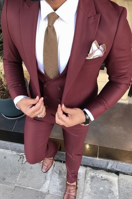 Man wearing a burgundy suit with a white shirt and patterned tie, standing outdoors.